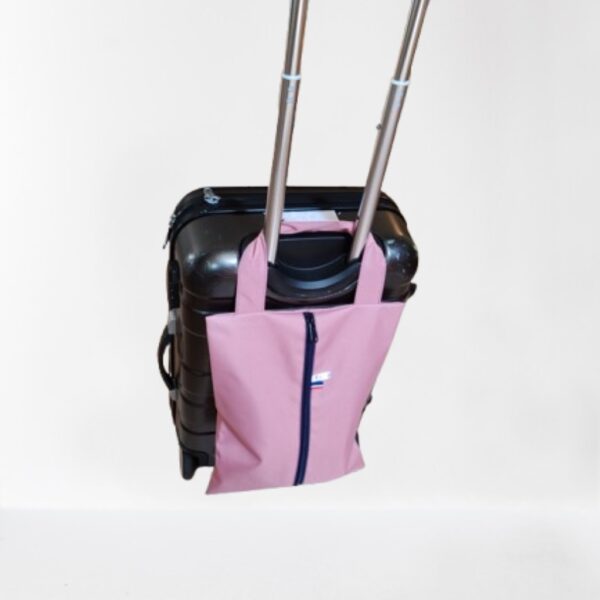 Sac à chaussures rose positionné sur la poignée pliable d'une valise